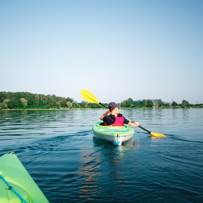 Person kayaking on a calm lake under a clear blue sky, showcasing Trillium Estates amenities with serene outdoor recreation opportunities.